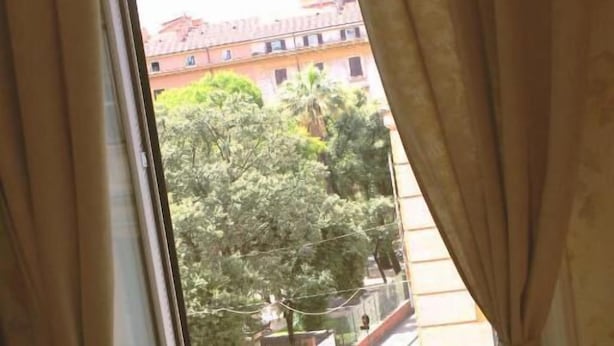 Una habitación con ventana, cortinas y una silla de madera.