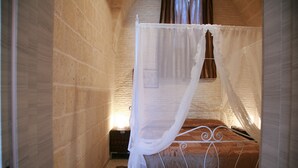 A single bed with a white metal frame and a brown quilt, a white canopy, and a small wooden chest beside it.