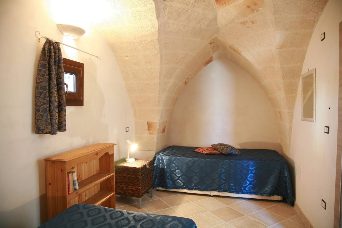 A small, cozy room with a sloped ceiling, a wooden nightstand, a single bed, and a small window.