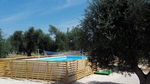 A pool area with a wooden deck, two green lounge chairs, and a tree.