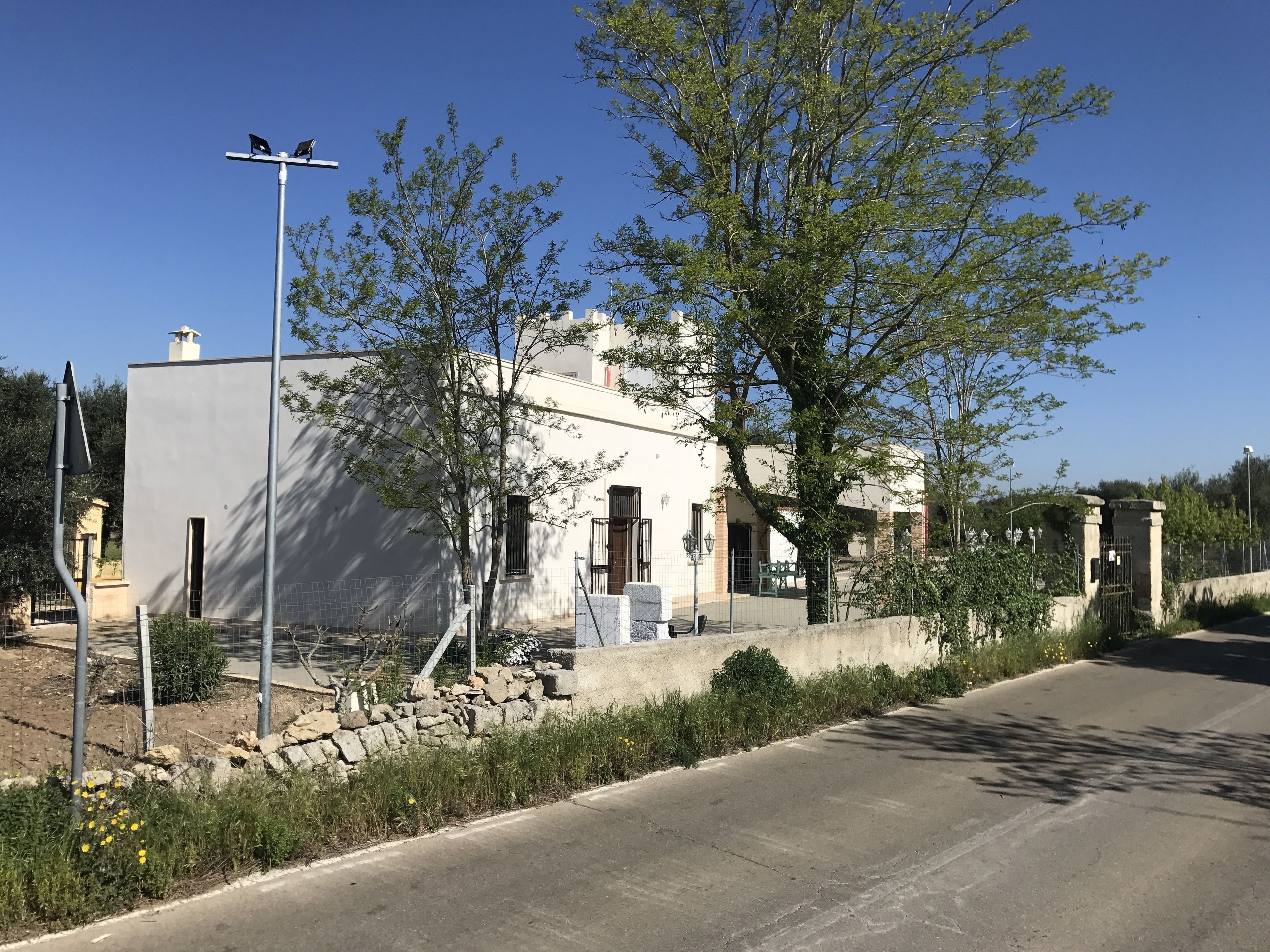 Ein zweistöckiges Gebäude mit weißer Fassade, einem gut sichtbaren Eingang und einem kleinen Gartenbereich mit Steinmauer und Pflanzen.