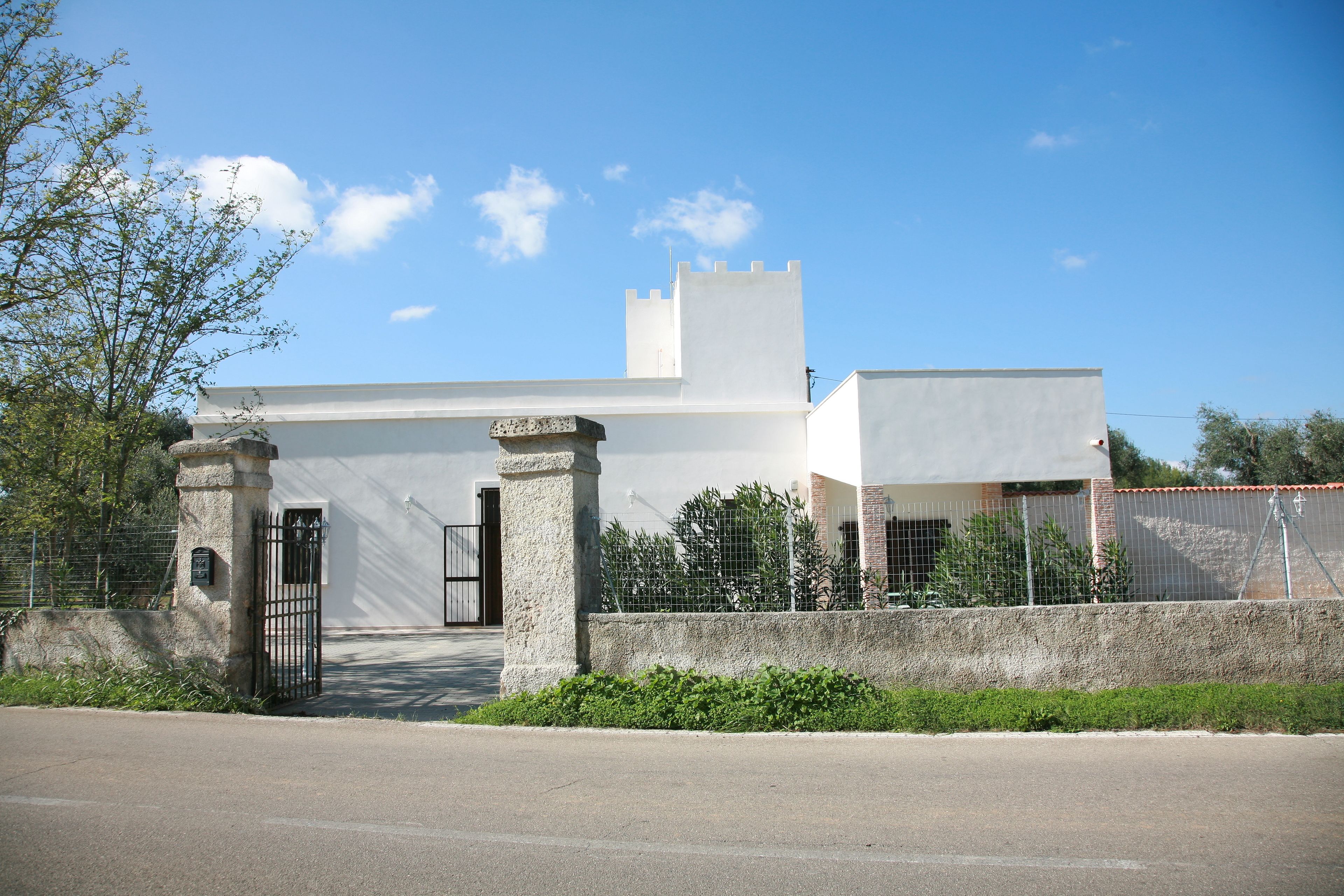 A white building with a gated entrance, a small tower-like structure, and a paved driveway.