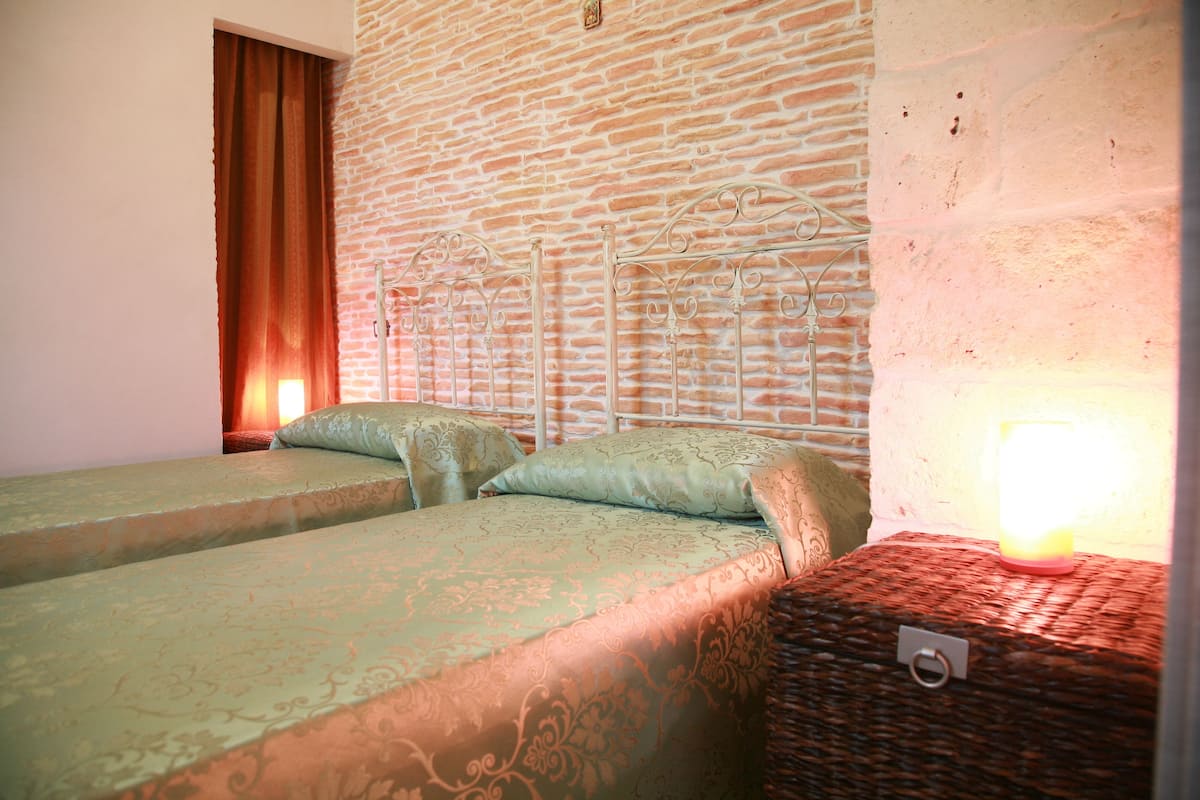 A room with two beds, a brick wall, and a lit lamp on a nightstand.