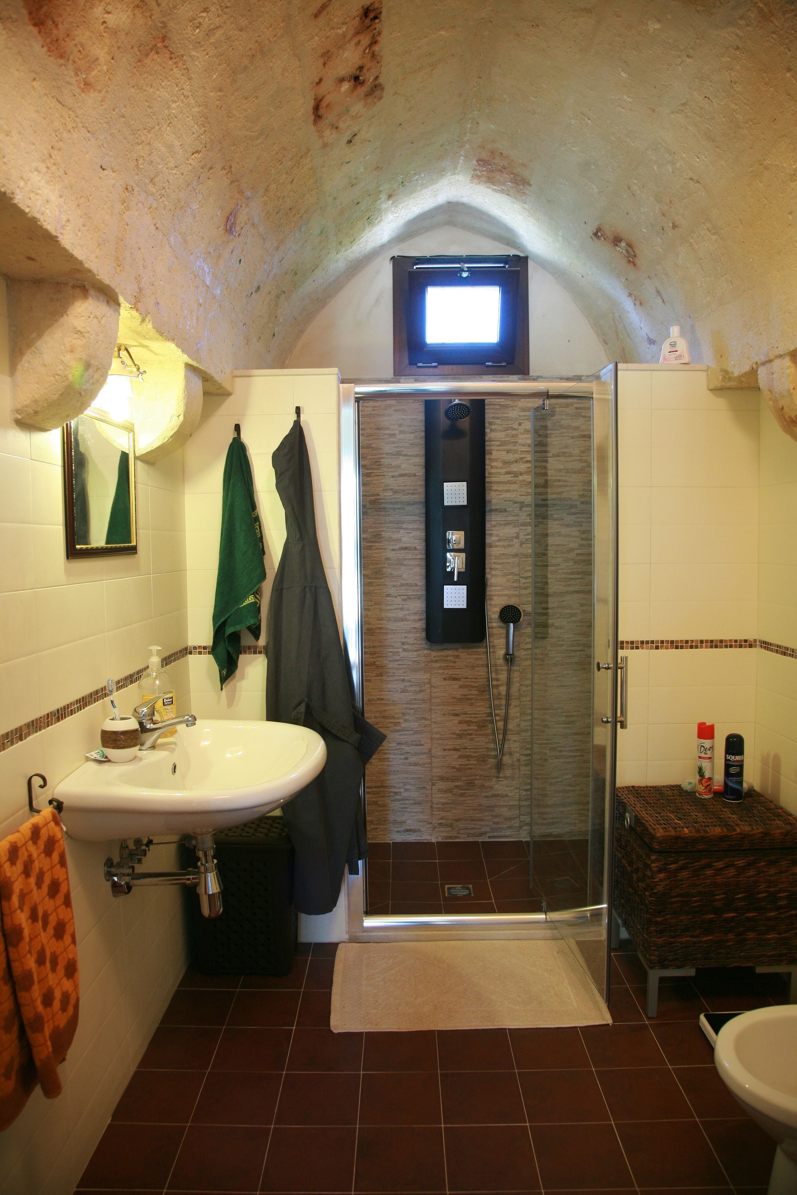 A bathroom with a sink, mirror, towel rack, shower, and a television mounted on the ceiling.