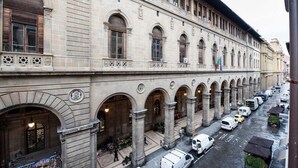 A historic building with a series of arches and columns, a covered walkway, and a street below with parked vehicles. - Repubblica (Florence)