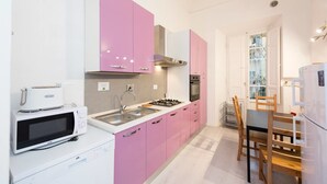 A compact kitchen with pink cabinets, a white countertop, a microwave, a stove, and a refrigerator. - Repubblica (Florence)