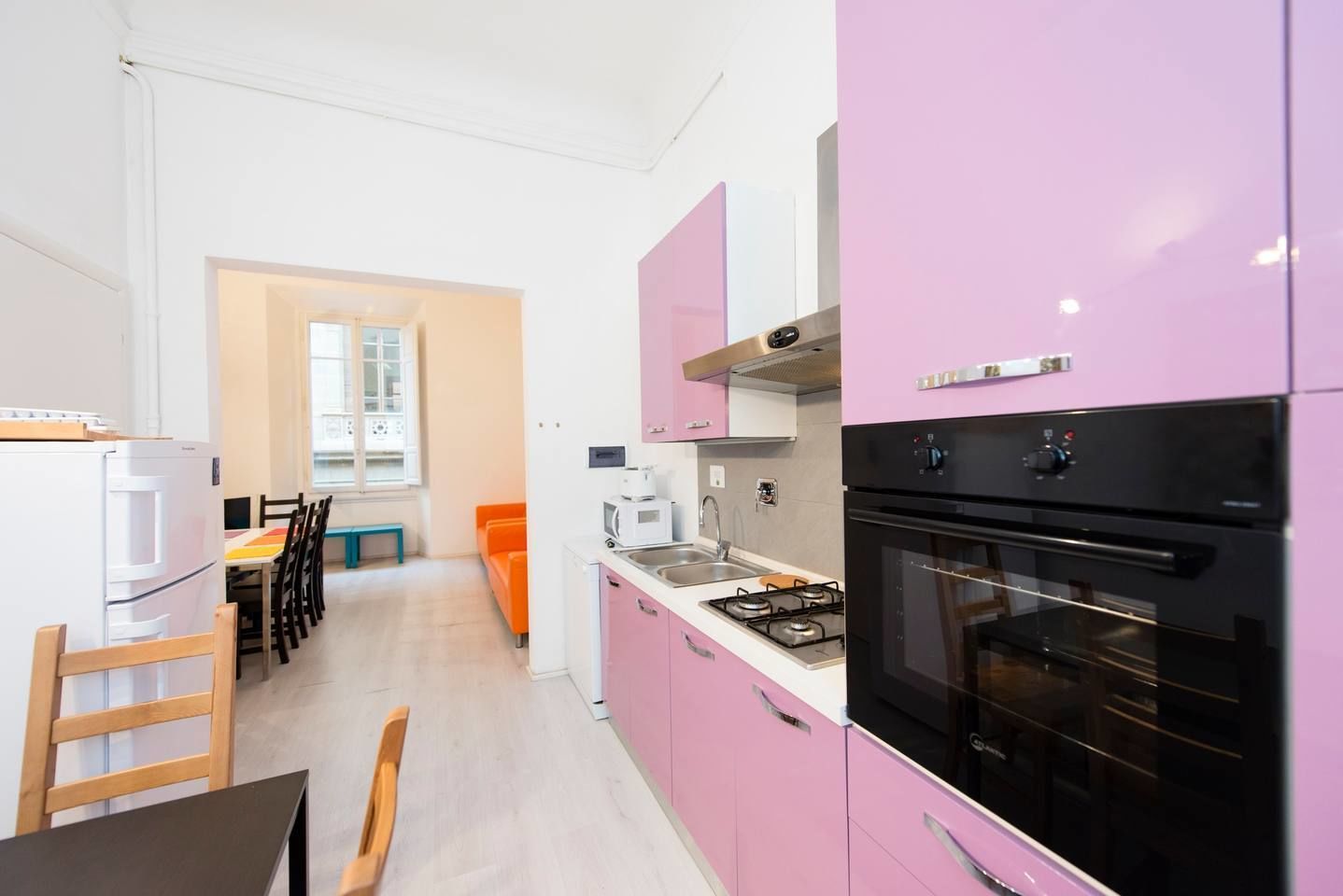 A modern kitchen with pink cabinets, a black oven, and a dining area with a table and chairs.