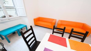 A room with a white table, black chairs, a turquoise bench, and two orange sofas. - Repubblica (Florence)
