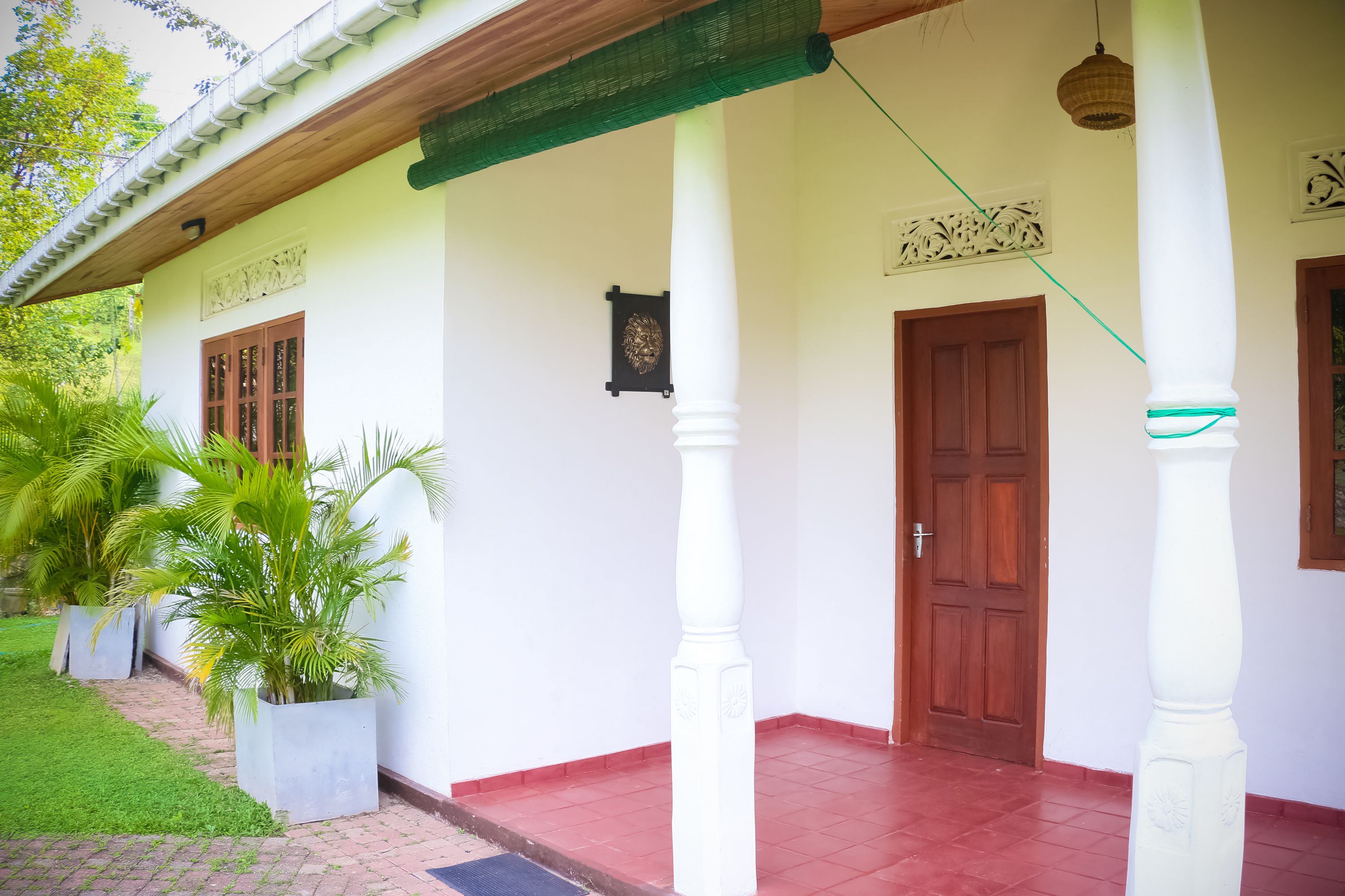 A white building with a red-tiled entrance, a wooden ceiling, and a green netting.