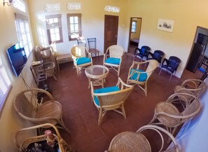 A spacious room with wicker furniture, a television, and a door leading to another room. - Horahena Farm Stay (Kaduwela)