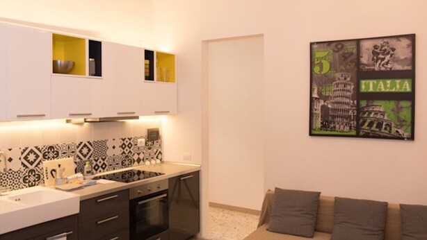 A modern kitchen with white cabinets, a black countertop, and a dining area with a white table and chairs. - Elisa Apartment (Florence)