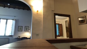 Habitació amb taula de fusta, finestra amb persianes, llum penjada a la paret i quadres emmarcados.