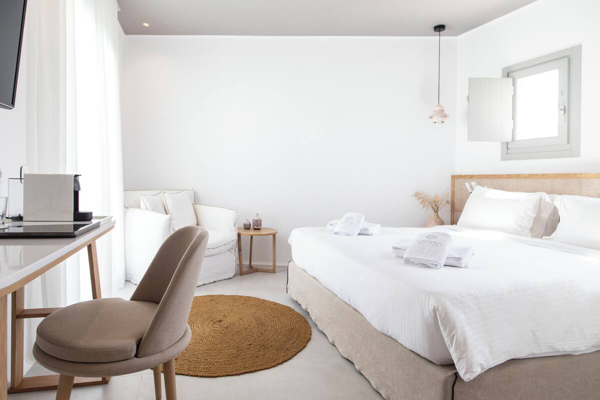 Una habitación de hotel moderna con una cama, un escritorio con una computadora portátil, una silla, una mesita y un tapete redondo.