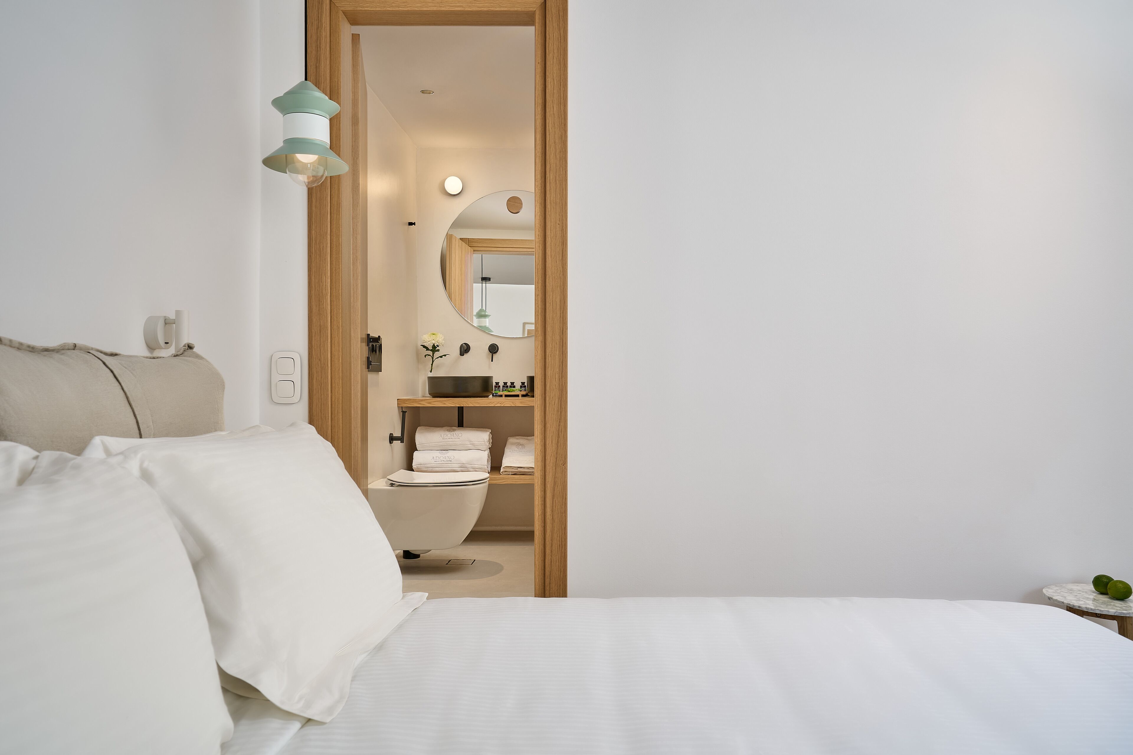 Une chambre à coucher comprenant un lit, une table de chevet, une commode, un miroir et une salle de bain visible à travers une porte ouverte.
