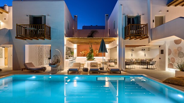 A swimming pool with lounge chairs and a sunbed, surrounded by a building with balconies and a covered outdoor seating area. - Adorno Beach Hotel & Suites (Mykonos)