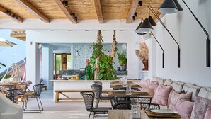 A modern dining area with wooden tables, black chairs, and a central plant. - Adorno Beach Hotel & Suites (Mykonos)