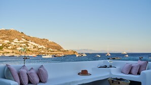 A seaside terrace with a white sofa, cushions, a hat, and a basket. - Adorno Beach Hotel & Suites (Mykonos)
