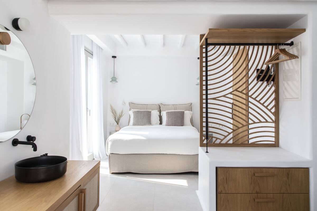Un dormitorio moderno con una cama grande, una mesita de noche de madera, un lavamanos redondo negro y un armario de madera.