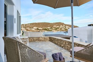 A balcony with wicker furniture, a stone floor, and a view of a coastal village.