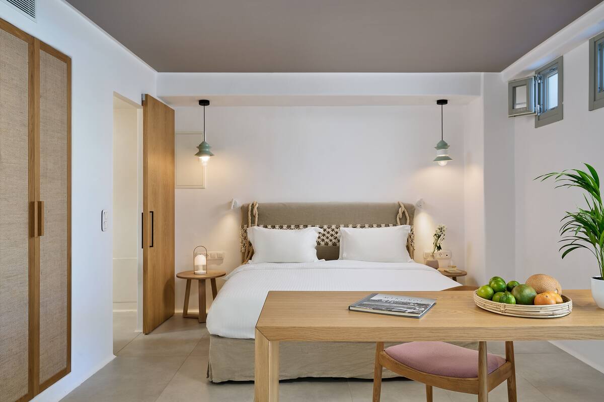 Un dormitorio moderno con cama, mesitas de noche, una mesa de madera con una cesta de frutas y una planta en maceta.