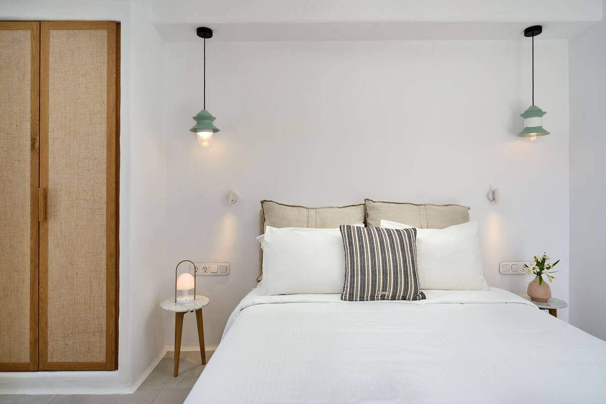Una cama bien tendida con ropa de cama blanca, dos lámparas de noche y una mesita con una lámpara al lado.