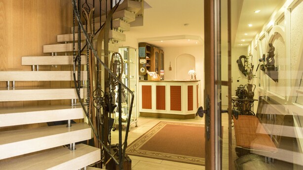 A modern interior with a wooden staircase, a reception desk, and a seating area. - Landhaus Fischer (Braunlage)
