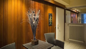 A room with wooden panel walls, a wicker chair, a table with a vase, and a door. - Landhaus Fischer (Braunlage)