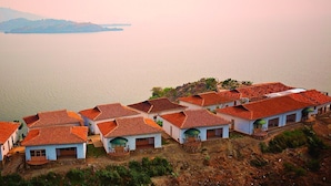 Ein Küstendorf mit Häusern mit Terrakotta-Dächern, einige davon mit Balkonen, und Blick auf das Meer und sanfte Hügel in der Ferne.