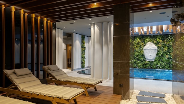 Un moderno espacio de spa con tumbonas de madera, una estatua de Buda y una piscina.