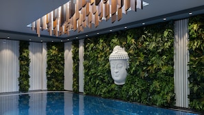 Un área de piscina interior moderna con piso de vidrio transparente, jardines verticales verdes y una escultura blanca decorativa.
