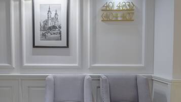 Una habitación con dos sillones grises tapizados, una fotografía en blanco y negro de un edificio histórico enmarcada, y un letrero con números colgado en la pared.