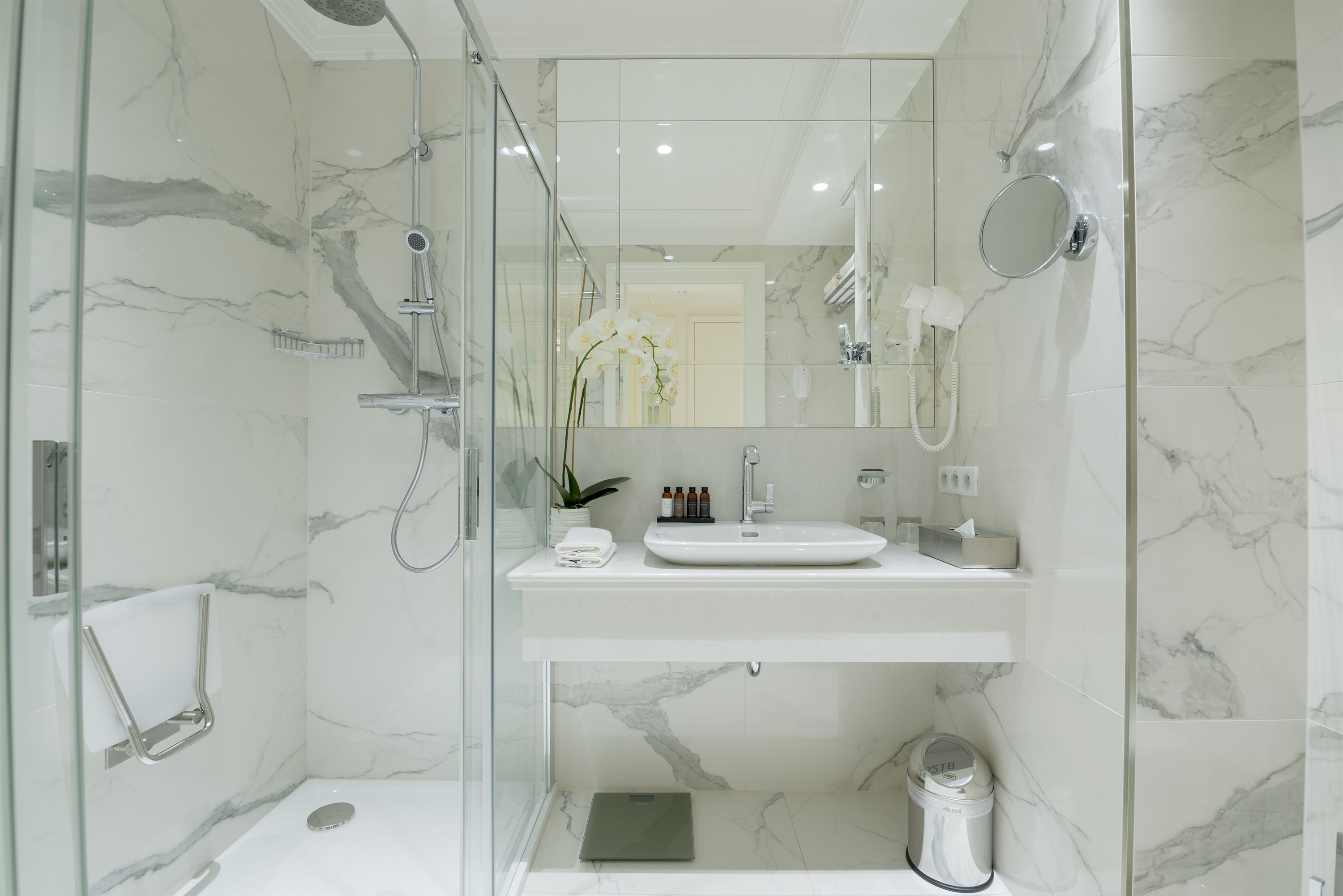 Une salle de bain moderne avec une douche à parois de verre, un lavabo blanc et un miroir.