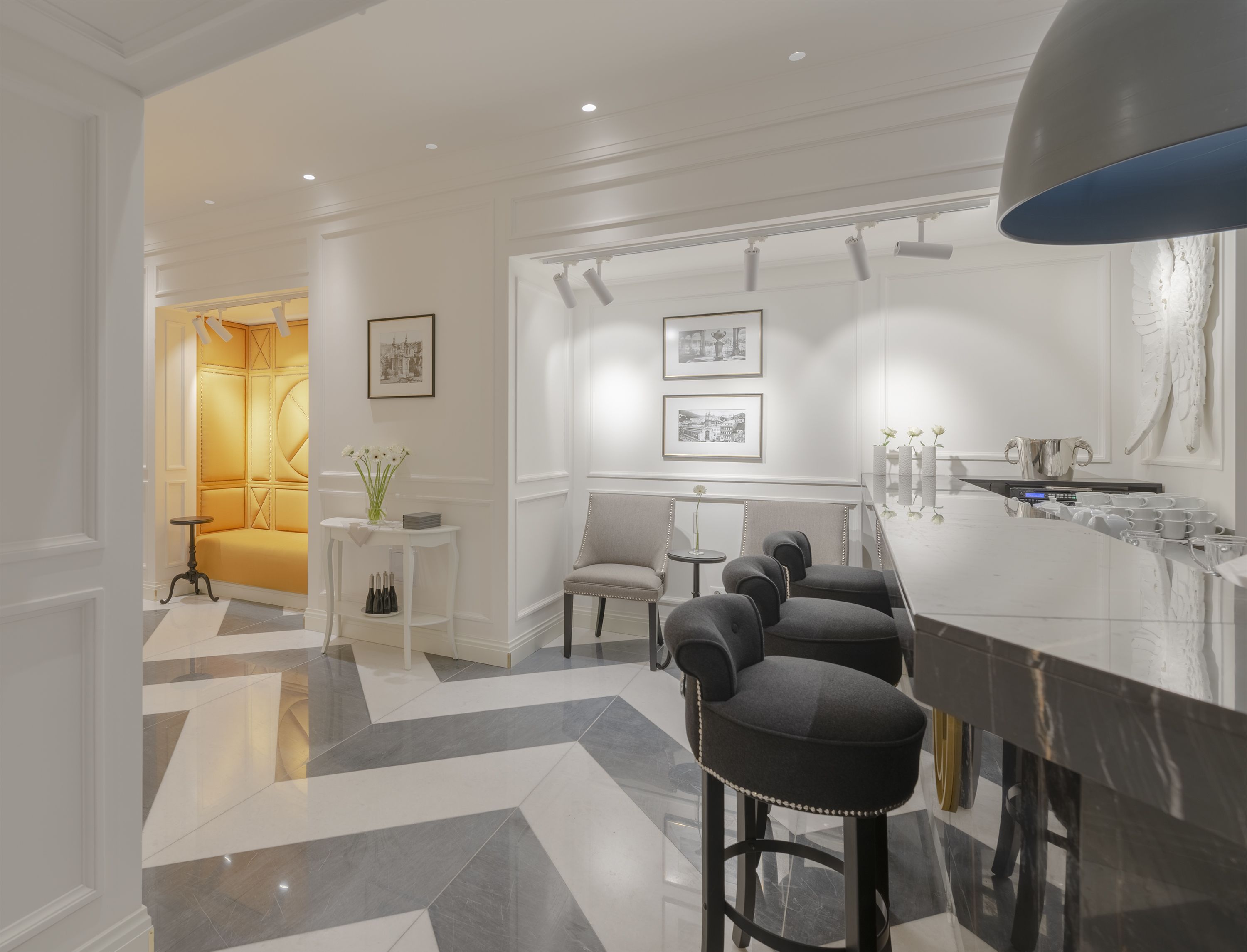 A modern kitchen with a marble countertop, bar stools, and a large pendant light.