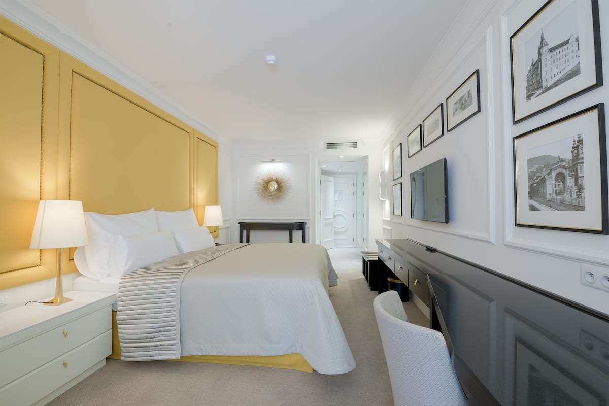 Een hotelkamer met een groot bed, nachtkastjes met lampen, een televisie en ingekaderde foto's aan de muur.