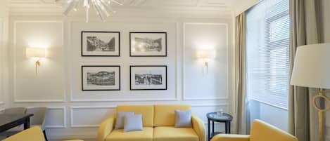 A modern living room with a yellow sofa set, a round glass coffee table, and framed black-and-white photographs on the wall.