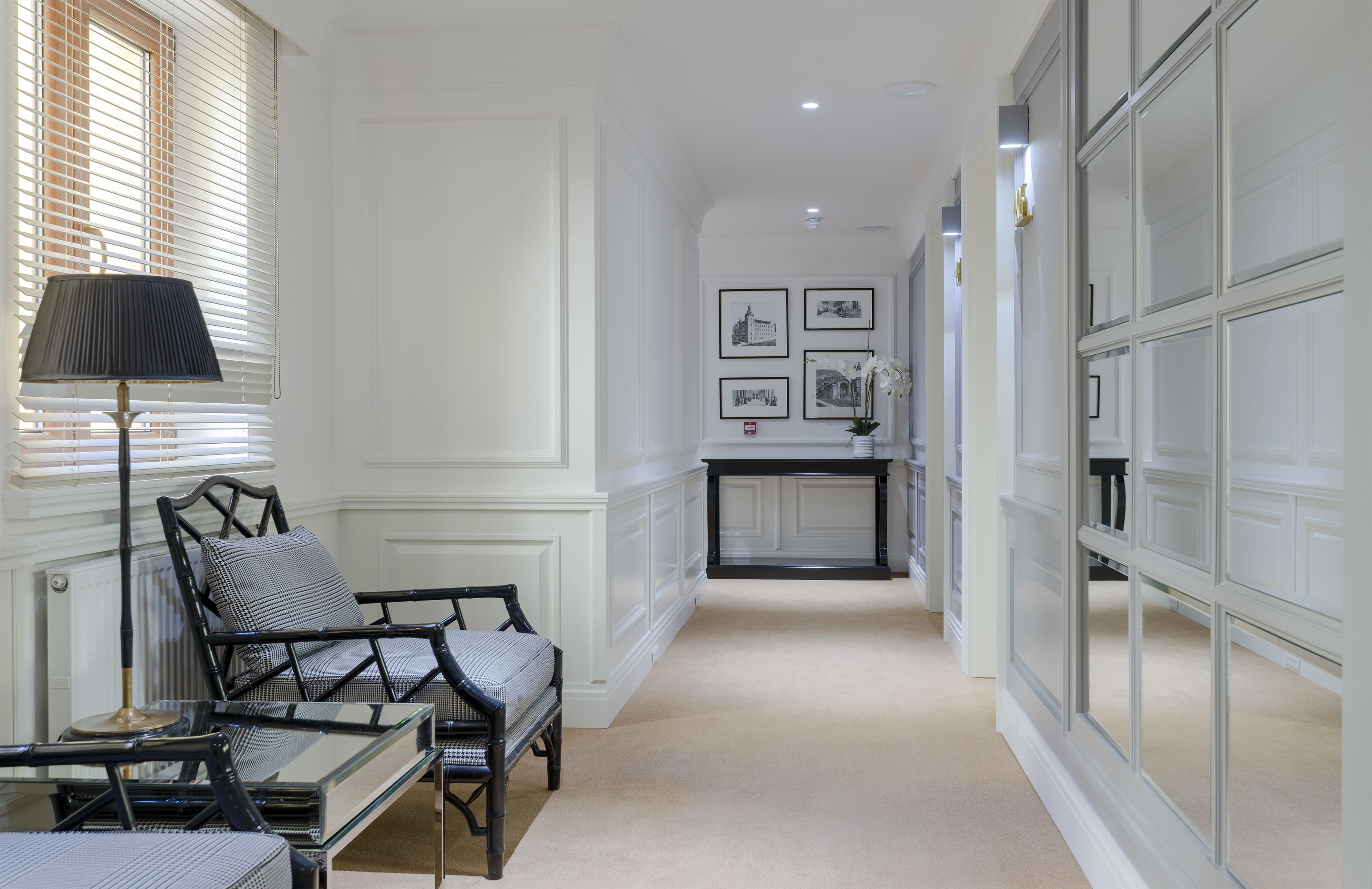 Un couloir avec un coin salon comprenant une table et des chaises, une lampe et des tableaux encadrés accrochés au mur.