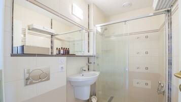 Un baño moderno con ducha envuelta en vidrio, un lavabo blanco y un espejo sobre él.