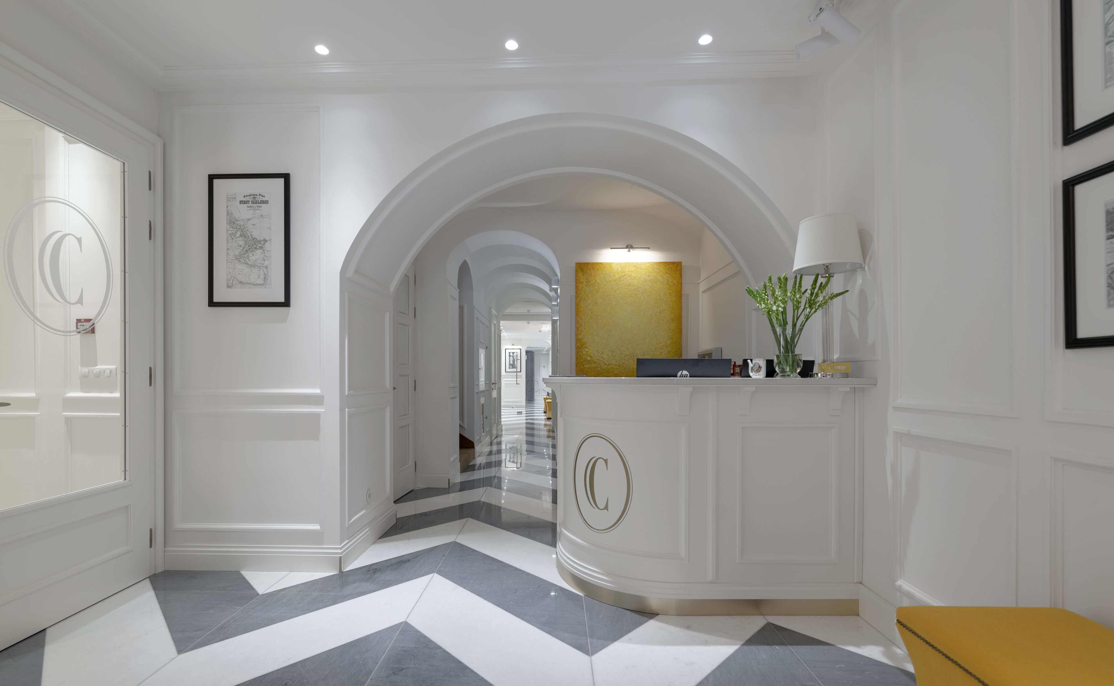 A hallway with white walls, a checkered floor, and a reception desk with a gold accent.