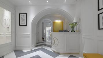 A hallway with white walls, a checkered floor, and a reception desk with a gold accent.