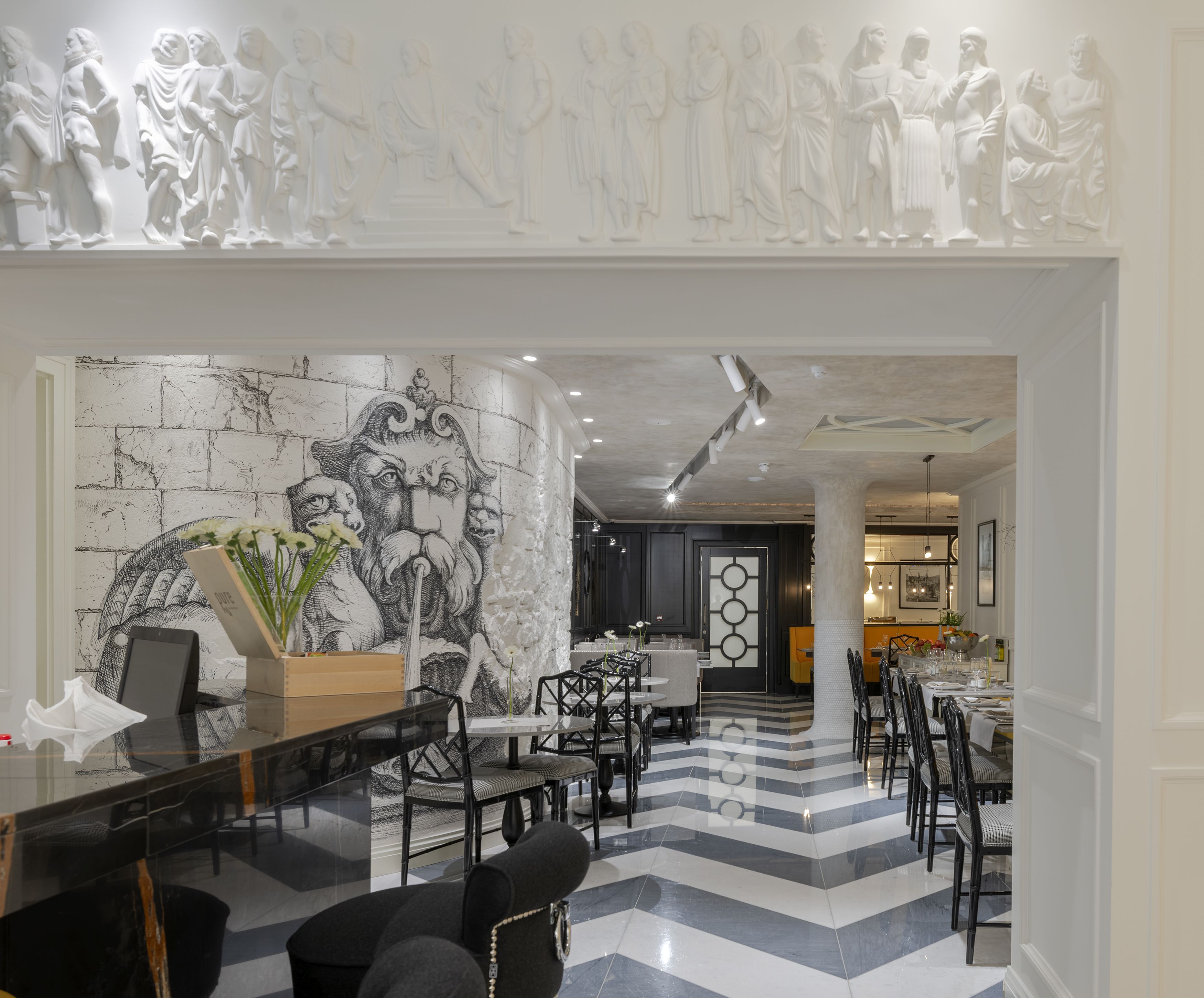 A modern hotel lobby with a marble floor, black and white striped pattern, and a large wall mural. There are dining tables and chairs arranged for guests.