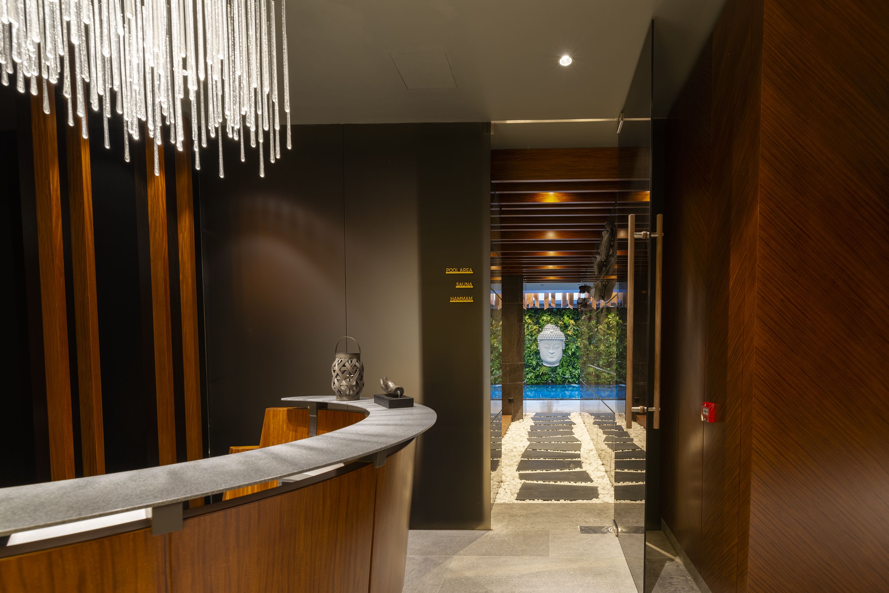 A reception area with a wooden reception desk, a modern light fixture, and a sign indicating the spa and sauna.
