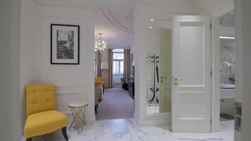 Un pasillo con un sillón amarillo, un cuadro enmarcado en la pared y una puerta que da al baño.
