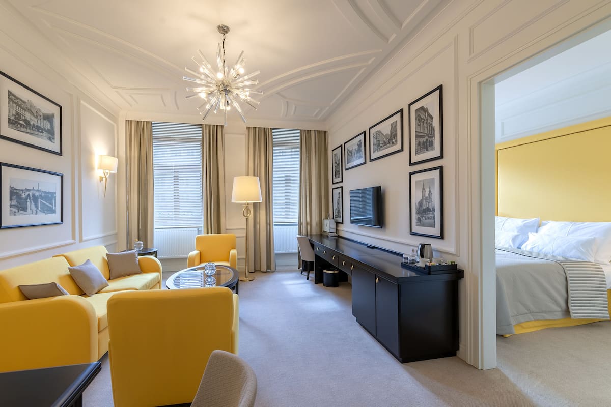 Een hotelkamer met een gele bank, een bureau, een bed en een kroonluchter.