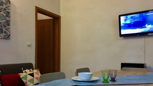 Un comedor con una mesa lista para dos personas, un televisor montado en la pared y una puerta que da a otra habitación.