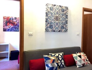 A living room with a grey sofa, red and patterned cushions, and two abstract paintings on the wall. - San Lorenzo (Florence)