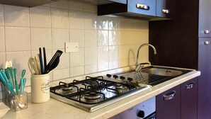 Una cocina con estufa a gas, pileta de acero inoxidable y alacenas.