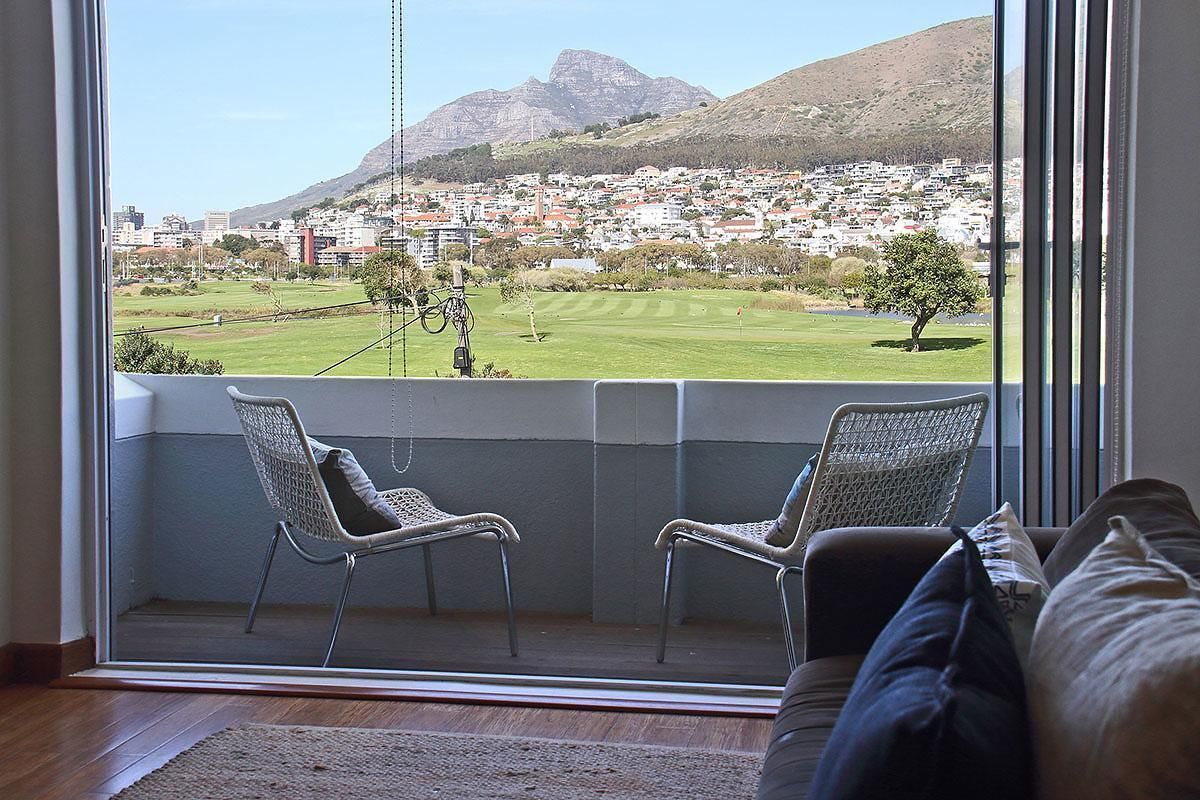 A balcony with two wicker chairs, a view of a town and mountains, and a glimpse of a golf course.