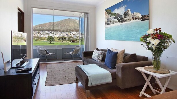 Ein modernes Wohnzimmer mit einer Couch, Fernseher und Blick auf eine Küstenlandschaft durch große Fenster.