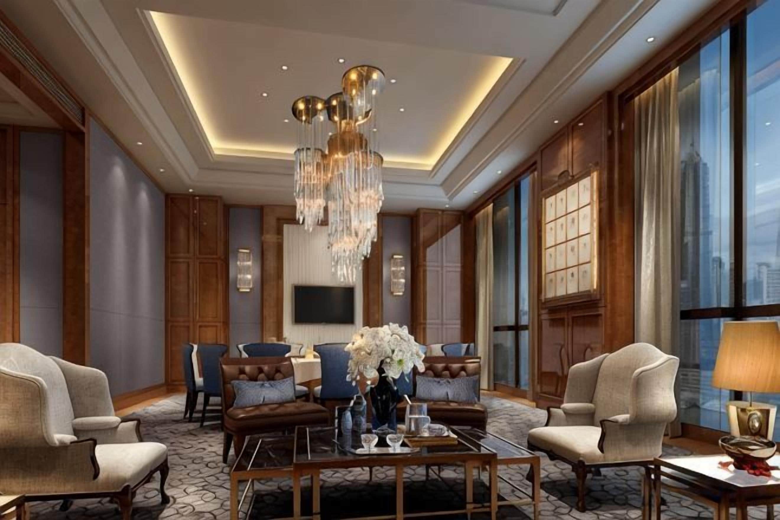 A spacious lobby with a high ceiling, a chandelier, comfortable seating, a large window, and a flat-screen TV.