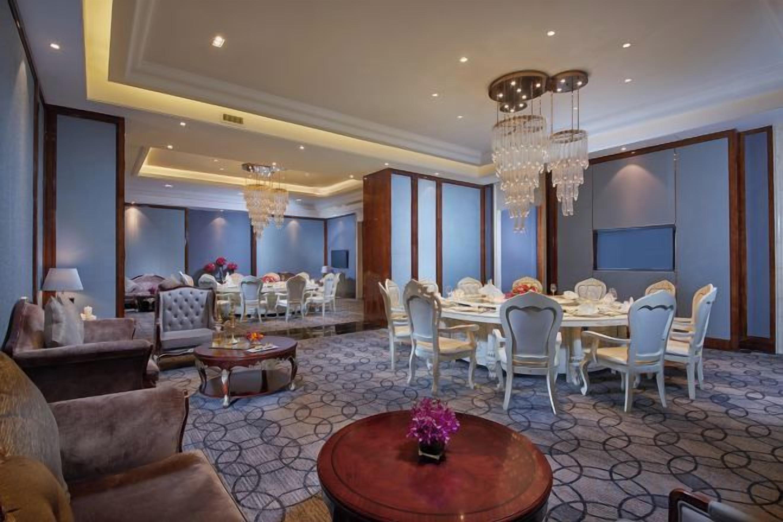 Un hall d’hôtel comprenant un espace repas, des coins salon et un lustre.